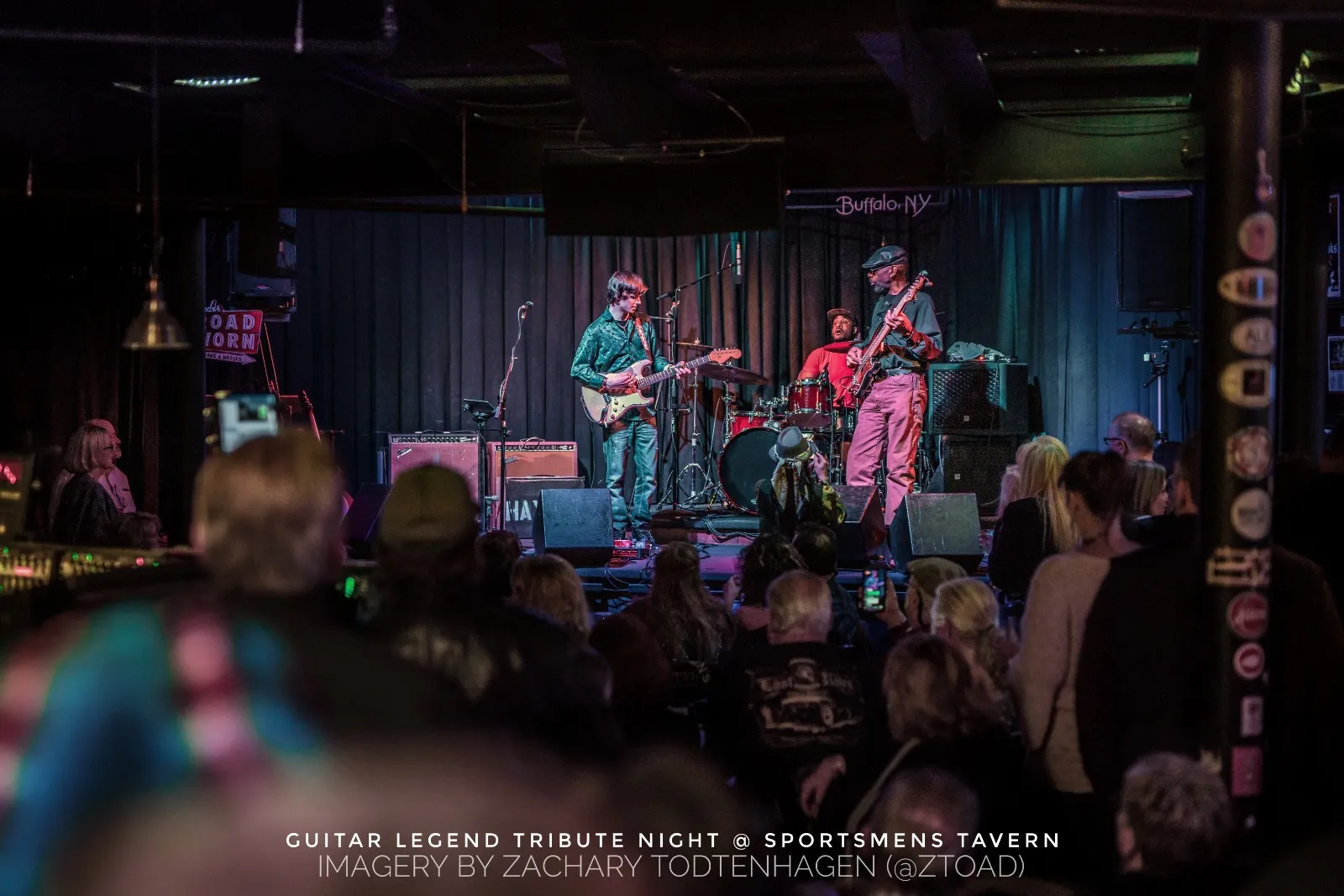 Wide view of the Hayden Fogle Band on the Sportsmens Tavern stage seen over the heads of a standing audience.