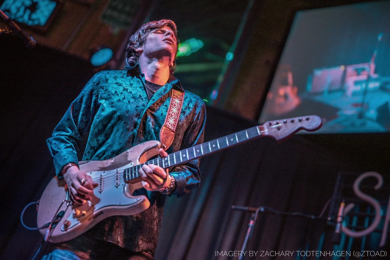 Hayden Fogle photographed from a low angle mid-solo, head tipped back, playing a heavily worn Fender Stratocaster.