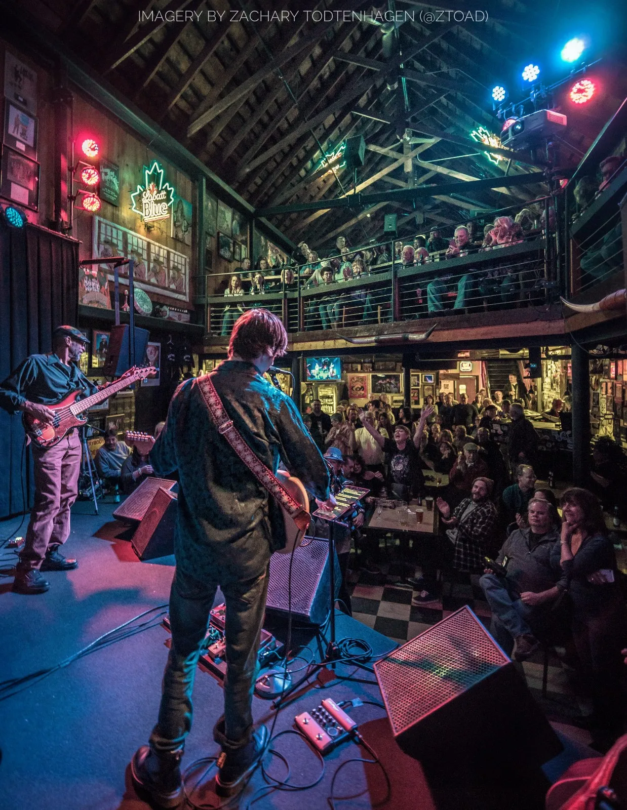 The stage seen from behind Hayden Fogle, looking out over the band and a packed crowd in the timber-framed room at Sportsmens Tavern.